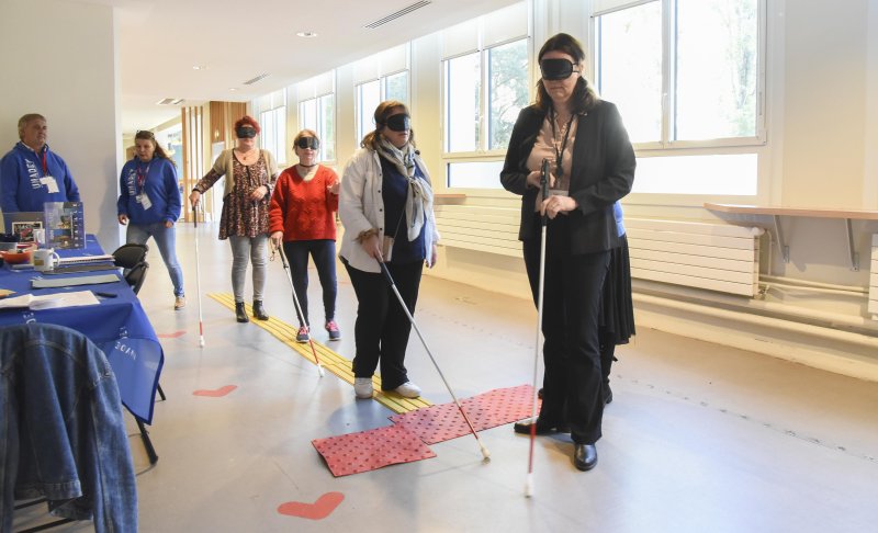 Des personnes portant un bandeau sur les yeux expérimentent la déambulationavec une canne blanche. 